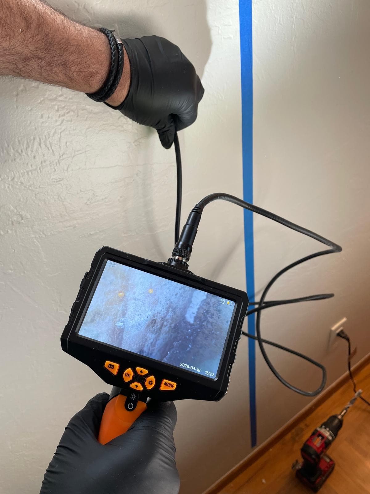 Inspector threading a borescope camera into a small wall cavity with visible mold shown live on the LCD screen