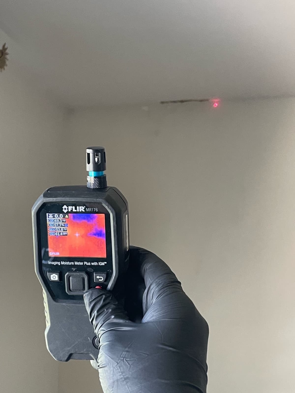 Inspector holding FLIR infrared imaging moisture meter up to a ceiling corner showing a live thermal scan